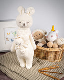 Karo the Softie Kangaroo Crochet Toy in front of wicker basket filled with crochet toys and greeting card in frame on top of brown blanket