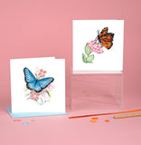 Quilled Blue Butterfly & Pink Flowers Greeting Card with light blue envelope next to monarch butterfly quilled greeting card on pink background