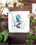 Quilled Colorful Seahorse Greeting Card hanging on a wooden wall behind an orchid and pink flowers.