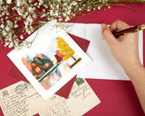 Quilled Cozy Autumn Cabin Greeting Card with dark red envelope next to hand writing insert and flowers
