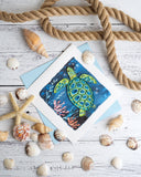 Quilled Decorative Sea Turtle Greeting Card on white wooden background with light blue envelope next to rope and sea shells