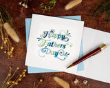 Quilled Happy Father's Day Card with light blue envelope next to insert with red pen and dried florals on brown background