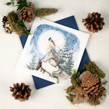Quilled Howling Wolf Greeting Card lays on a sparkly white backdrop, besides pinecones and moss.