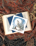 Quilled Howling Wolf Greeting Card lays on an open book above a patterned scarf.