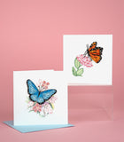 Quilled Monarch Milkweed Butterfly Greeting Card and Quilled Blue Butterfly & Pink Flowers Greeting Card in front of a pink background.