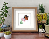 Quilled Monarch Milkweed Butterfly Greeting Card in a Golden Square Artist Series Frame on a wooden surface surrounded by books succulents and terrarium.
