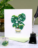 Quilled Monstera greeting card with green envelope in front of plant on green background