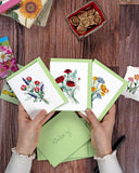 Quilled Wildflower Note Card Box Set cards being help above wooden background, light green envelopes, wax seals, flower seeds, and the Quilled Wildflowers Gift Enclosure Mini Card.