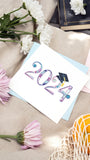 Quilled 2024 Grad Card on picnic blanket with flowers books and bag of oranges