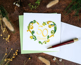 Quilled 50th Wedding Anniversary Card with light green envelope next to insert with red pen surrounded by dried florals