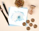 Quilled Abstract Nautilus Greeting Card laying flat on a cream background, surrounded by wax pellets, wax seals, a press, a letter opener, and a pen.