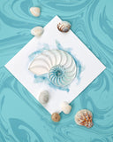 Quilled Abstract Nautilus Greeting Card laying flat on a ocean background, surrounded by seashells.