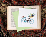 Quilled Bicycle & Flower Basket Greeting Card on top of open book with light green envelope on paisley background
