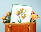 Quilled Bird of Paradise greeting card nested in bamboo bag surrounded by yellow flowers in front of a light blue background