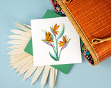 Quilled Bird of Paradise greeting card coming out a bamboo bag laying on tom of a dried palm frond on top of a light blue background