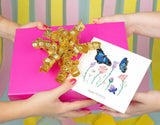Quilled Birthday Flowers & Blue Butterflies Greeting Card being passed with a pink birthday gift with a golden ribbon.