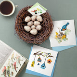  Quilled Bluebird & Babies Greeting Card on blue table next to nest with eggs on it and pamphlet of birds