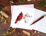 Quilled Cardinal & Cherry Blossom Greeting Card with pink envelope next to open insert with red pen surrounded by dried florals on brown background