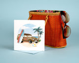 Quilled Classic Woodie Greeting Card standing up in front of a light blue background and a camel colored Hand-woven Bamboo Bag.