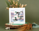quilled duck migration greeting card with dark green envelope next to dried florals on green background