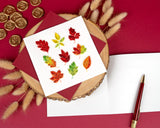 Quilled Fall Foliage Leaves Greeting Card with burgundy envelope on top of open card insert with pen and dried florals on red background