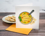 quilled get well soup greeting card with orange envelope in front of plate with saltines in front of white background