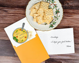quilled get well soup greeting card with orange envelope, insert with handwritten note, next to saltines on plate on wooden background