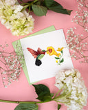 Quilled Hummingbird & Yellow Flowers Greeting Card with green envelope next to white flowers on pink background