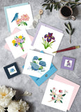 Quilled Iris Flower Greeting Card surrounded by other floral quilled greeting cards on table with pen, coffee, and flowers