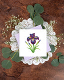 Quilled Iris Flower Greeting Card with lilac envelope on top of eucalyptus and baby's breath, on top of white lace doily on brown table