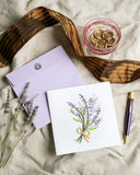 Quilled Lavender Bunch Greeting Card with purple envelope on beige fabric next to brown ribbon, wax seals, purple pen, and dried lavendar