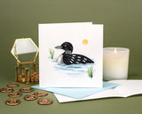 Quilled Loon greeting card standing up with light blue envelope on dark green background with wax seal stamps