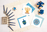 Quilled Modern Menorah Hanukkah Card next to Star of David Quilled Greeting card and quilled dreidel greeting card on table next to gifts and menorah
