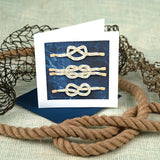 Quilled Nautical Knots Greeting Card standing in front of a knit background, surrounded by rope and fishing nets.