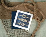 Quilled Nautical Knots Greeting Card laying down on a knit background, surrounded by rope and fishing nets.