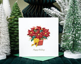Quilled Potted Poinsettia Holiday Card standing up with green envelope in front of christmas tree decor with green background