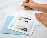 Quilled Snow Covered Trees Greeting Card laying on table with light blue envelope next to hand writing on the insert of the card