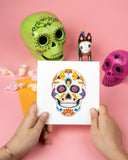 Quilled Sugar Skull Greeting Card being held in front of candy, sugar skulls, on pink background