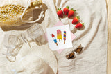 Quilled Summertime Treats Greeting Card on picnic blanket surrounded by hat, glasses, fruit, and bottle with drink