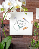 Quilled Thank You Healthcare Greeting Card hung on a wooden wall, next to a white orchid, a vase of pink flowers, and the Quilled Bromeliad Macrame Hanger Gift Enclosure Mini Card.