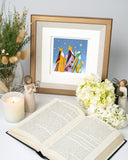 Quilled Three Wise Men Greeting Card in golden frame in front of open book next to flowers, angel statue, and candle
