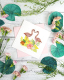 Quilled Tropical Flamingos Greeting Card with pink envelope on white background next to flowers, and paper decoration lilly pads
