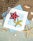 quilled starfish greeting card with blue envelope surrounded by shells on beige background