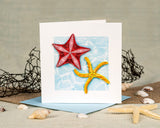 quilled starfish greeting card with blue envelope surrounded by shells on beige background