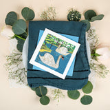 Quilled Two Swans Greeting Card with blue envelope on blue napkin and plate with florals
