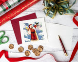 Quilled Vintage Santa Christmas Card with card insert and dark red envelope next to christmas gift wrapping paper and red ribbon