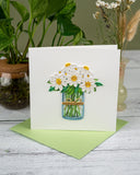 quilled daisy greeting card with green envelope on white wooden background with dried flowers and plant