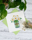 Quilled white daisy greeting card with green envelope on white wooden background with dried flowers and plant