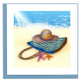 Blank greeting card featuring a quilled design of a beach bag and hat laying in the sand