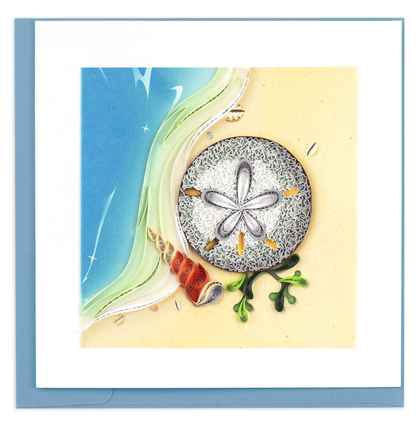 Blank greeting card of a quilled sand dollar sitting on a sandy  beach with waves crashing next to it.